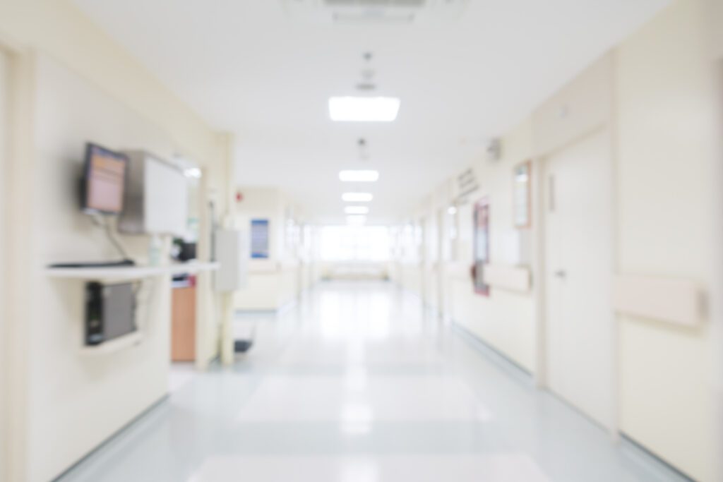 A softly blurred hospital hallway, evoking the long hours families spend caregiving