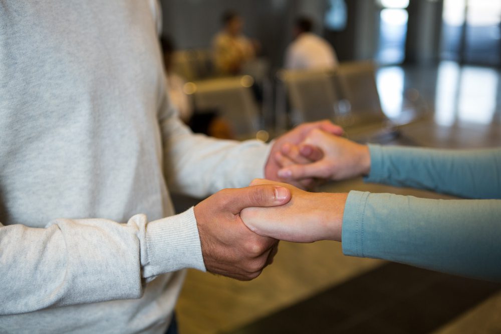 Two people holding hands in a quiet waiting area, offering each other support