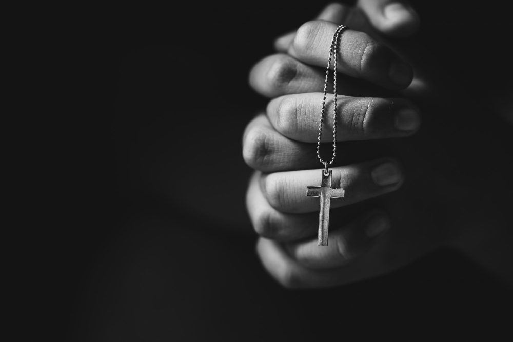 Hands holding a small cross in prayer, a symbol of faith and strength