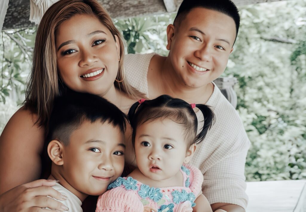 A smiling family portrait of Laureen “Love” Jamero-Lejarde with her husband and two young children, outdoors with greenery in the background.