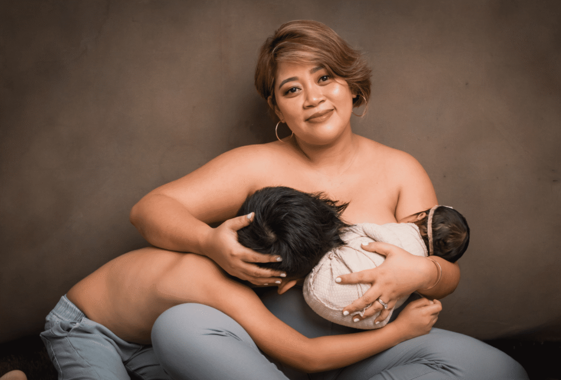 A mother sits with a serene smile while holding her two children—one breastfeeding and the other leaning close—capturing the intimacy of motherhood and family bonding.