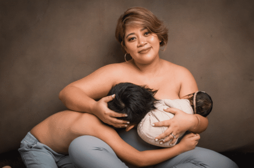A mother sits with a serene smile while holding her two children—one breastfeeding and the other leaning close—capturing the intimacy of motherhood and family bonding.