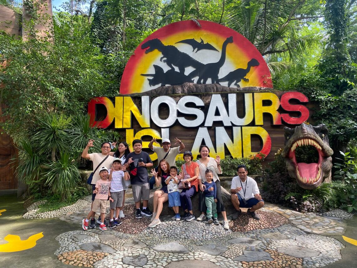 Family group posing in front of the Dinosaurs Island entrance sign in Clark, Pampanga