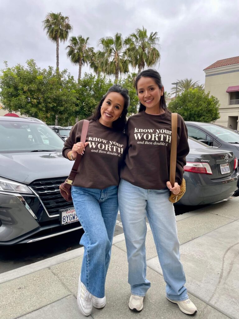 Two women wearing She is Rooted and Rising "Know Your Worth and Then Double It" brown sweatshirts in California.