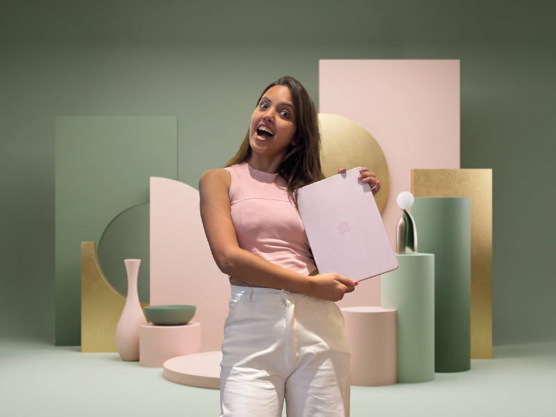 Nancy Gupta laughing and holding a laptop against a set of pink, gold and sage design elements