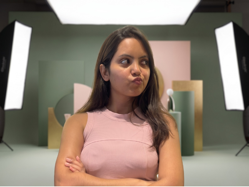 Nancy Gupta with arms crossed looking to the side in a studio set with pink and sage geometric shapes